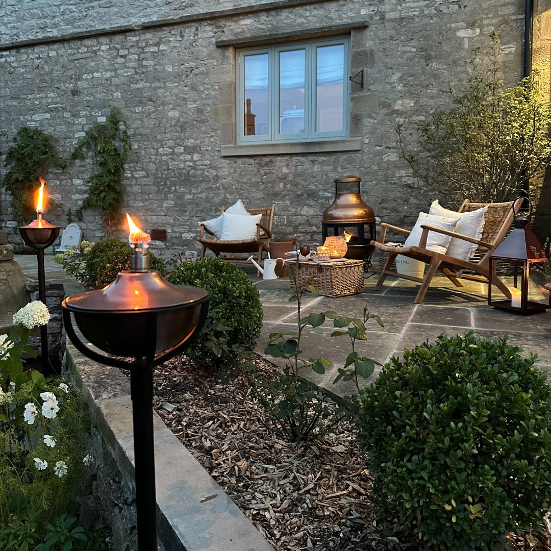 Garden lighting setting, with oil torches, fire pit and rattan chairs on flagstone floor patio. How can I light my garden without electricity?