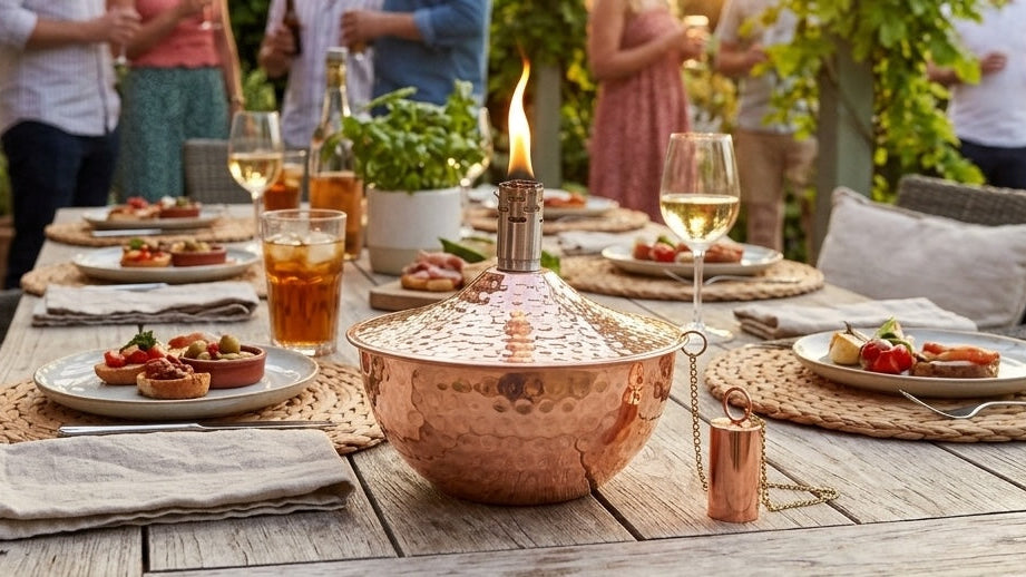 garden oil lamp in copper on summer garden dinner table with food and guests gathered behind with drinks