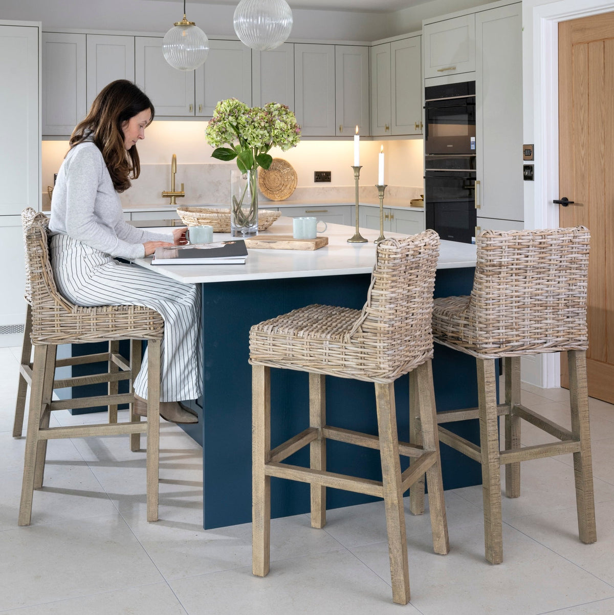 modern kitchen with island, lady sat at island with rattan kitchen stools