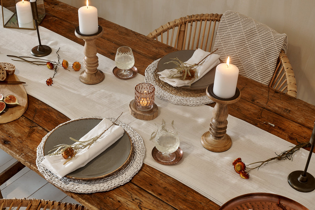 Christmas gift ideas, festive table setting with Christmas candlelight on cotton runner, with white rattan place mats, dinner plates and rattan chair with cushion