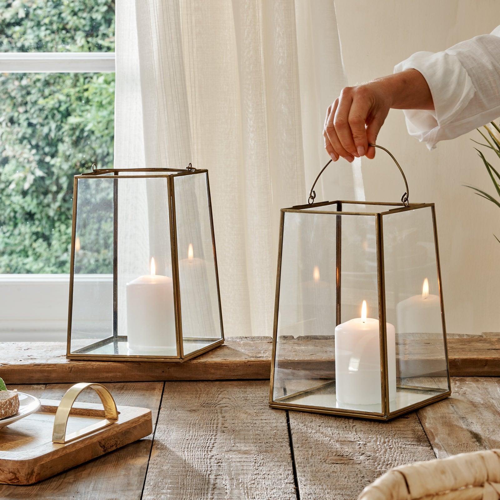 Vintage brass metal lanterns with hand, on wooden table with tray, in front of curtain