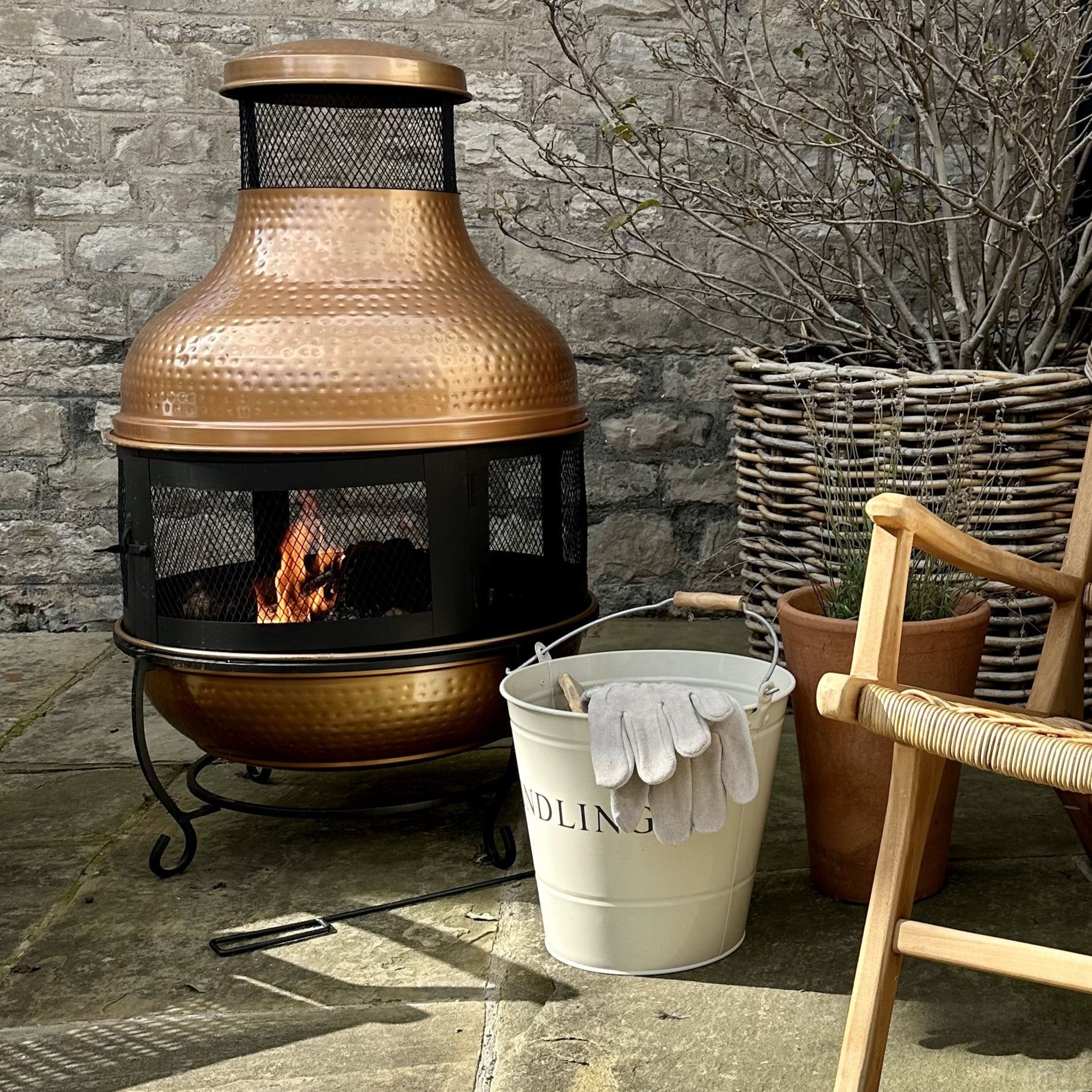 Copper Fire Pit outside on patio with fire bucket and rattan armchair