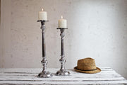 Silver pillar candle holders on white table with hat