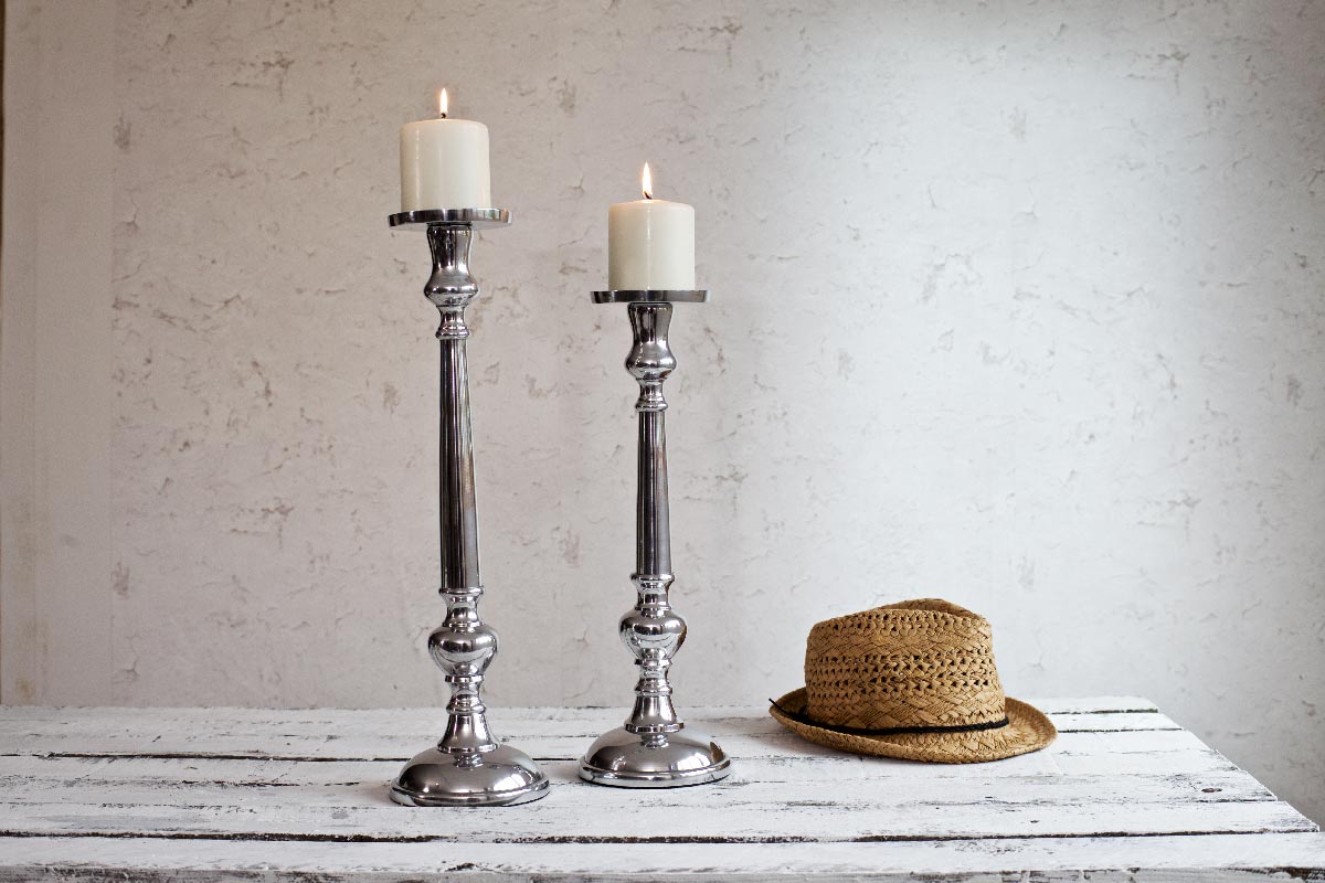 Silver pillar candle holders on white table with hat