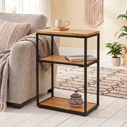 A three shelf side table with a black metal frame and mango wood shelves, styled next to a sofa.