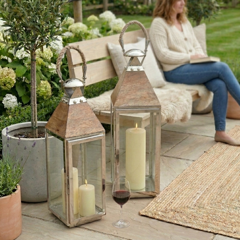 tall silver lantern in garden by plants and bench, lady having drink