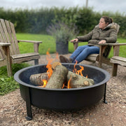 black fire pit on garden patio with lady relaxing in chair