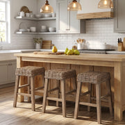 A rustic wooden kitchen island with three woven wicker bar stools in a bright, modern kitchen setting.