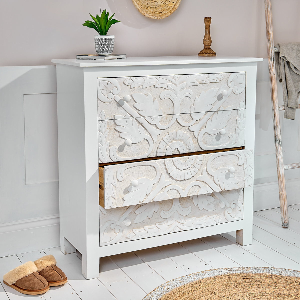 White bedroom chest of drawers with carved design next to wicker rug and wall ladder