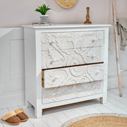 White bedroom chest of drawers with carved design next to wicker rug and wall ladder
