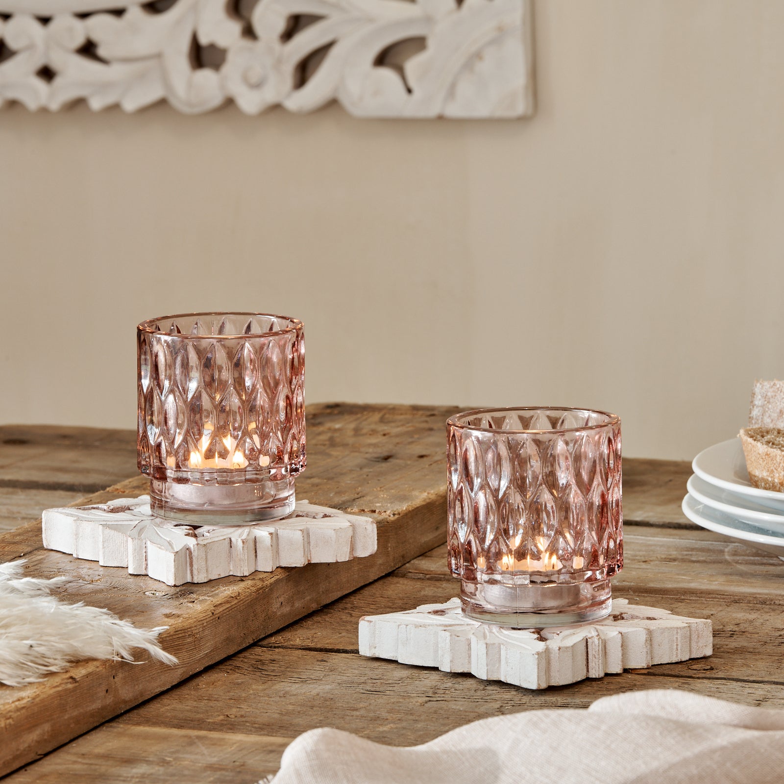 Vintage looking glass tealight holder on wooden table, with shite carved coasters and plates
