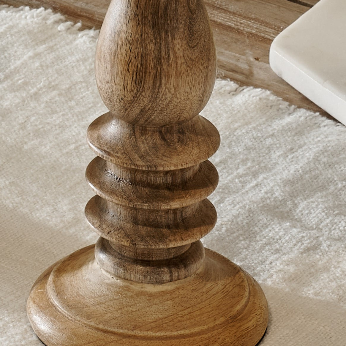 Close up of base of dark wood candle holder on cotton runner