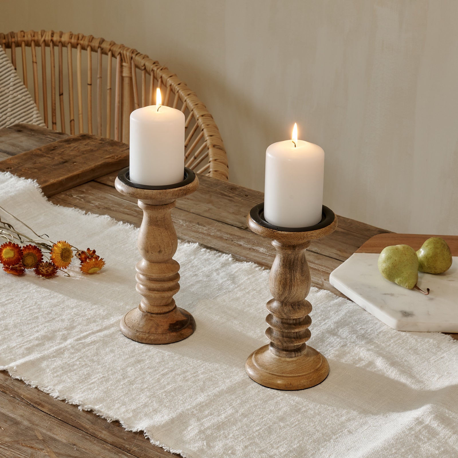 Wooden candle holders on cotton runner on wooden table, with chopping boards and rattan chair