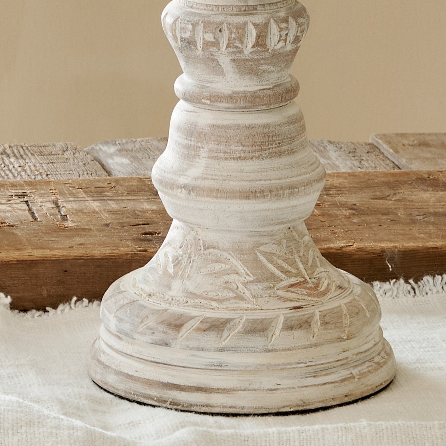 Close up of base of distressed tall white candlesticks on cotton runner on wooden table