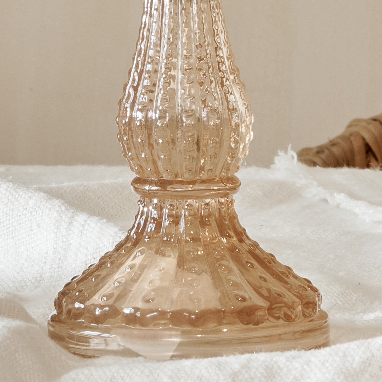 Close up of base of pink glass candlestick on cotton runner