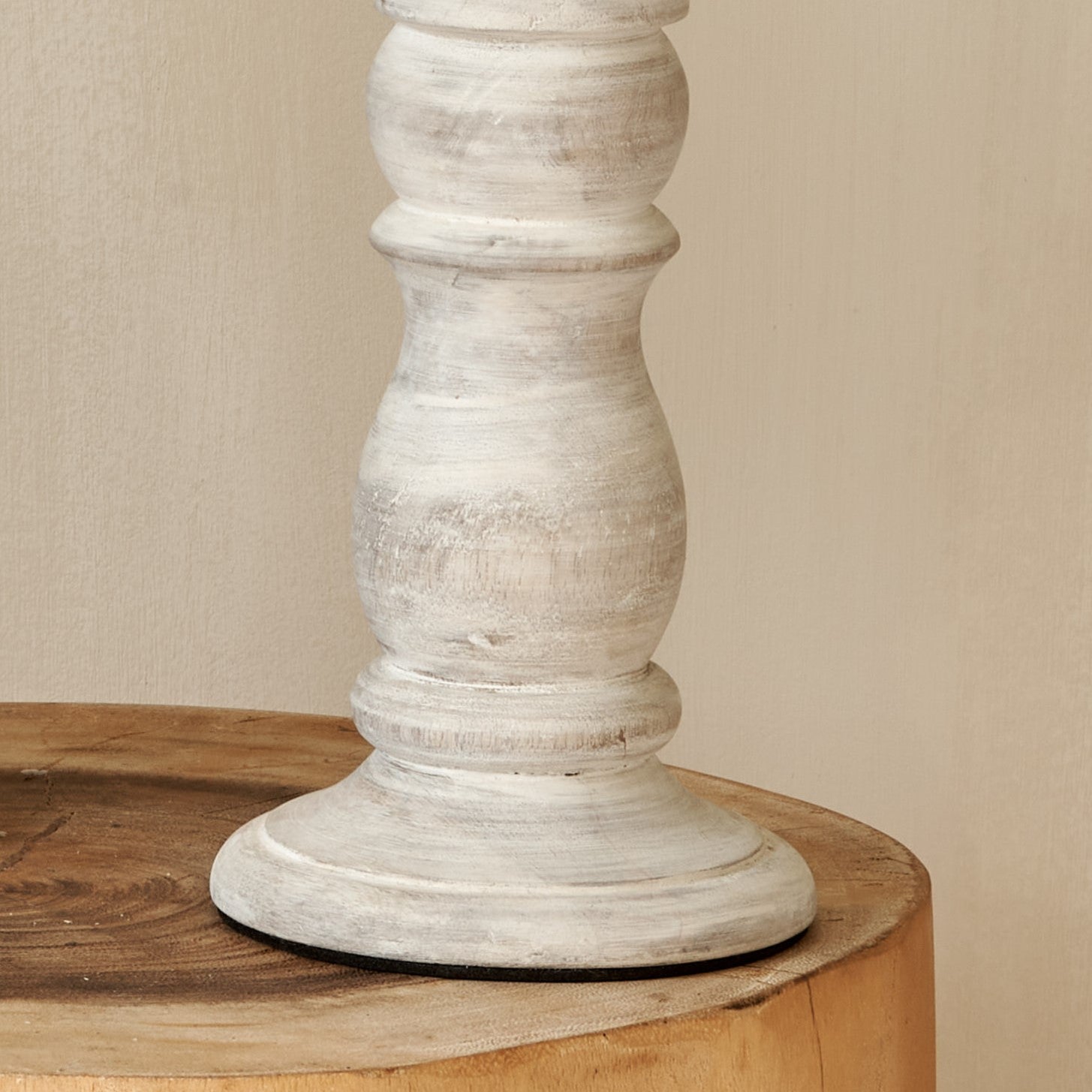 Close up of base of white wooden candlestick on log table