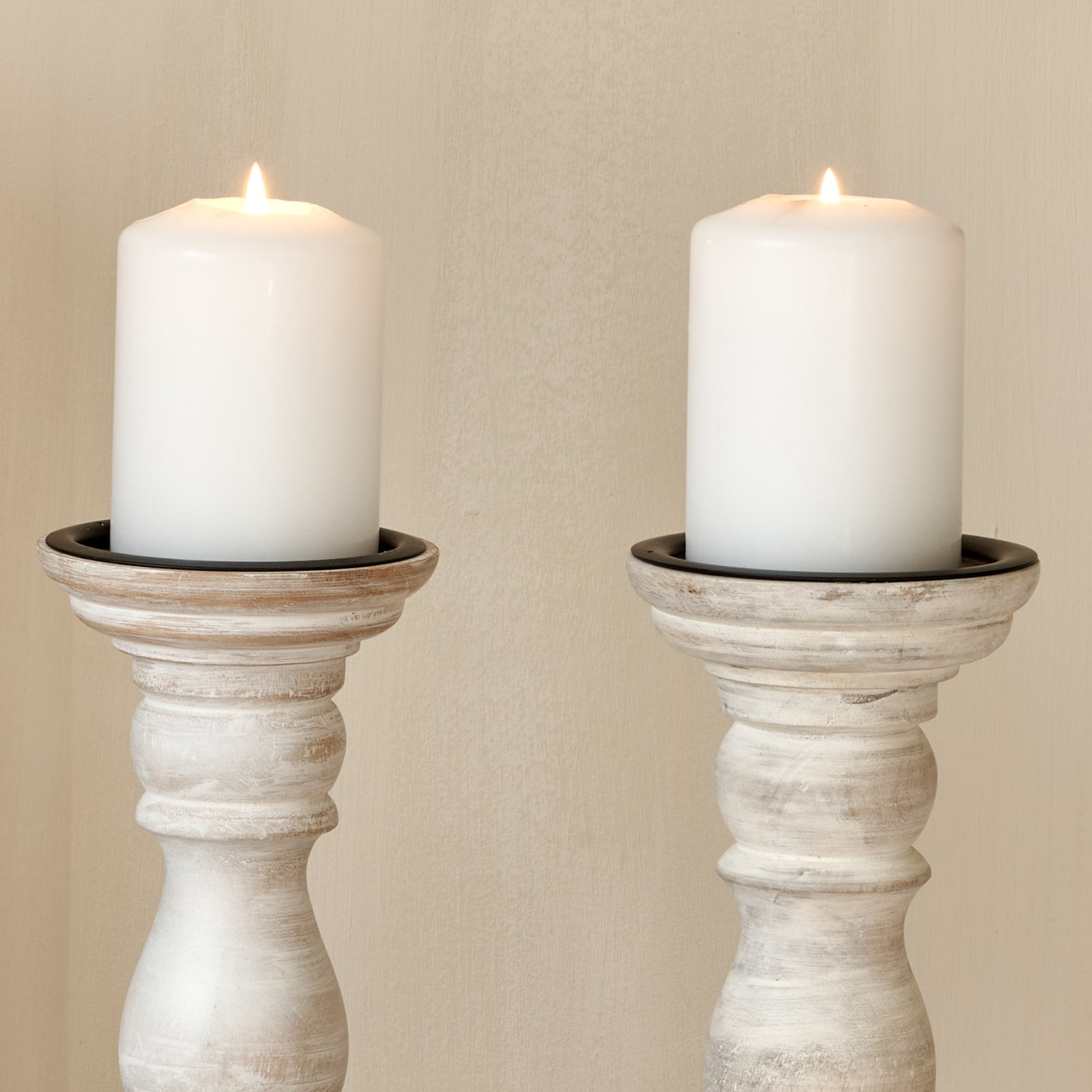 Close up of 2 white wooden candlesticks with white pillar candles