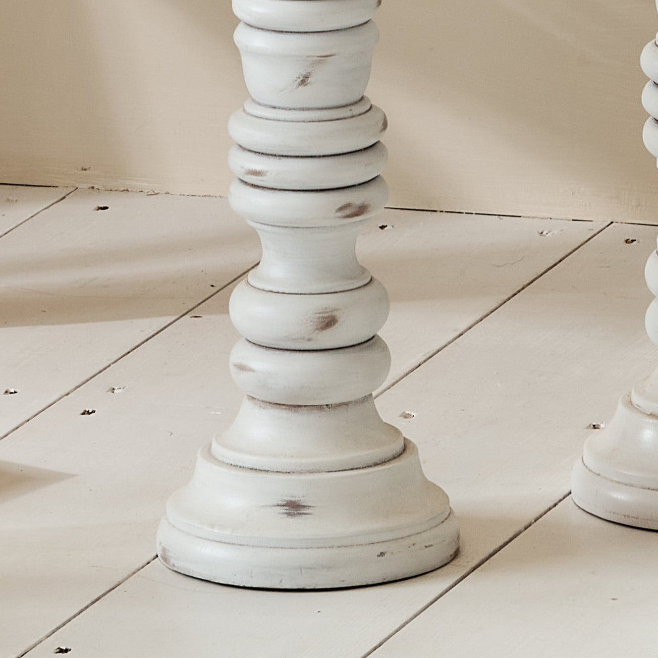 Close up of tall white candlestick on white wooden floor
