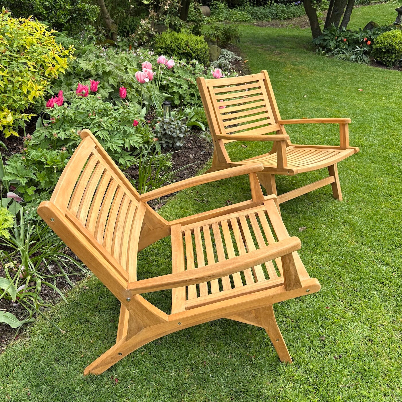 two wood garden chairs on grass with flowers in background