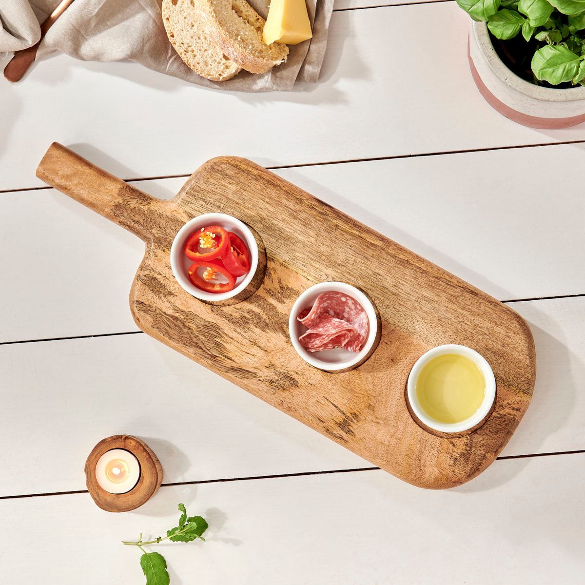 Rustic serving board with bowls on white wooden table with candle