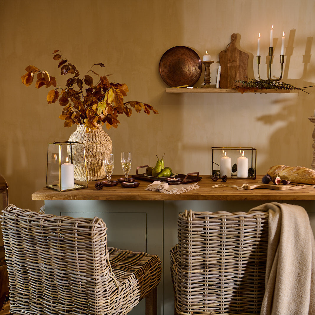 A rustic dining room scene with a kitchen island, wicker kitchen stools, candlelight, and food set at the table for entertaining