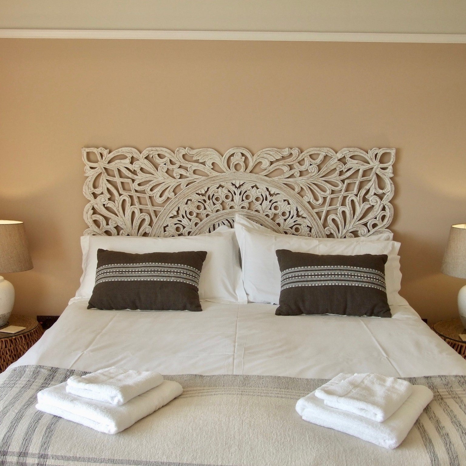 White Carved Wooden Headboard behind bed with cushions and towels