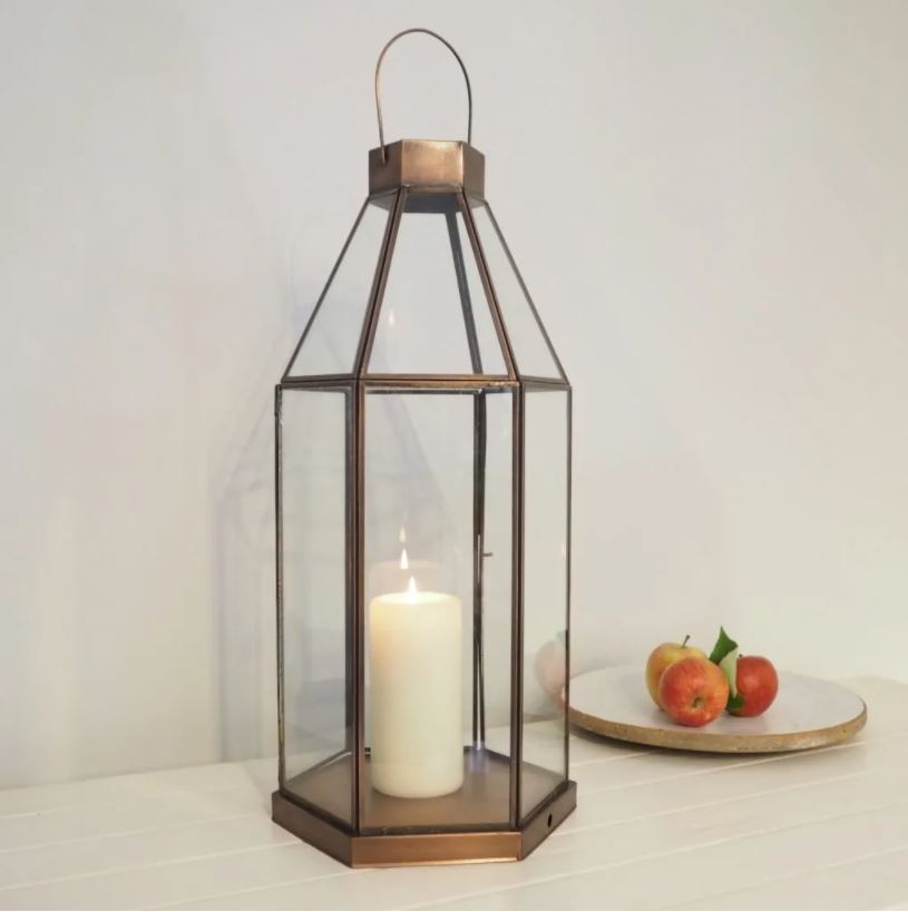 Hexagonal brass lantern on white table with bowl of fruit