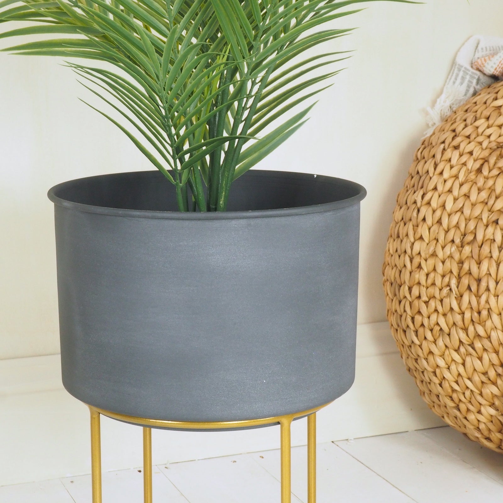 Slate grey plant pot with green plant and wicker pouffe in background
