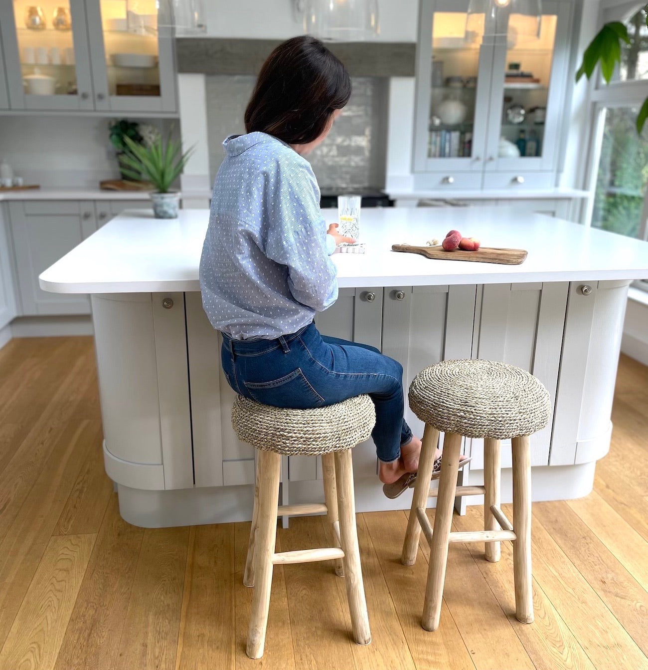 lady sat at her marble kitchen island on wicker kitchen stools, drinking a glass of water