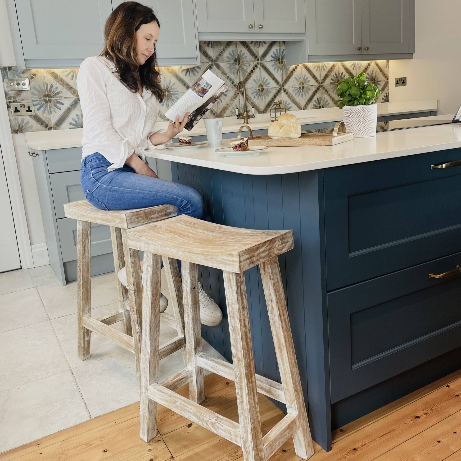 Woman sat reading on whitewashed bar stool on blue kitchen island