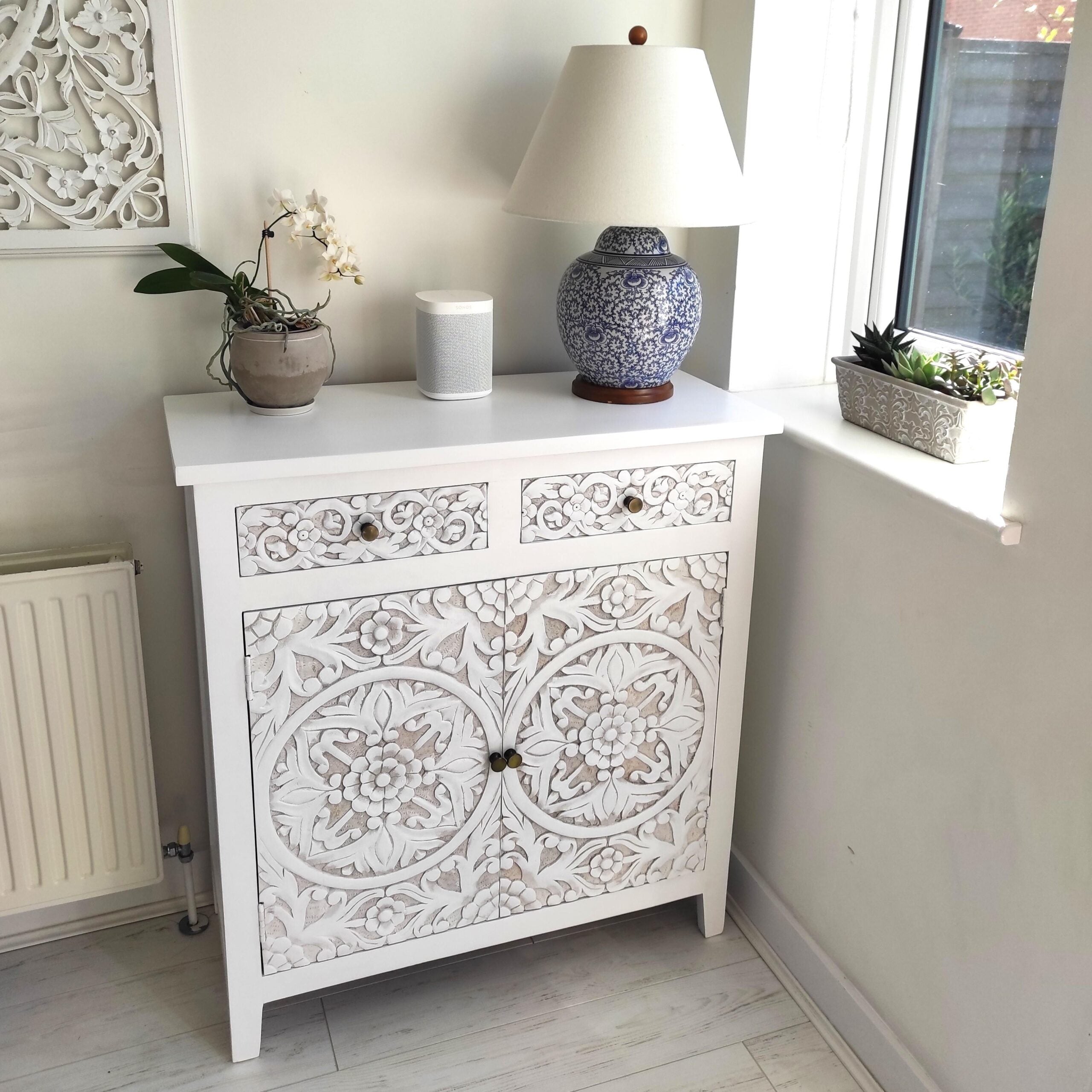 Carved Wooden Sideboard on wooden floor by window, with potted plant and lamp