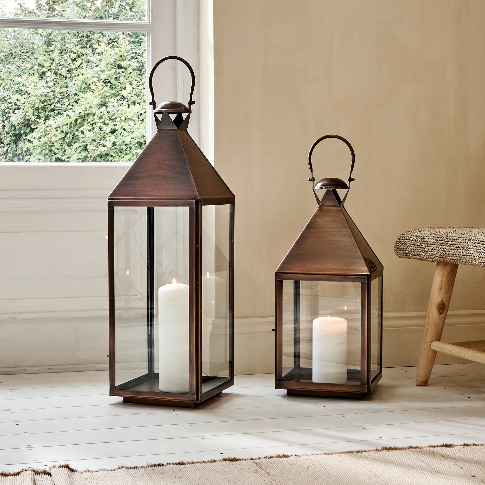 Aged copper candle lanterns on wooden floor with rug, in front of window
