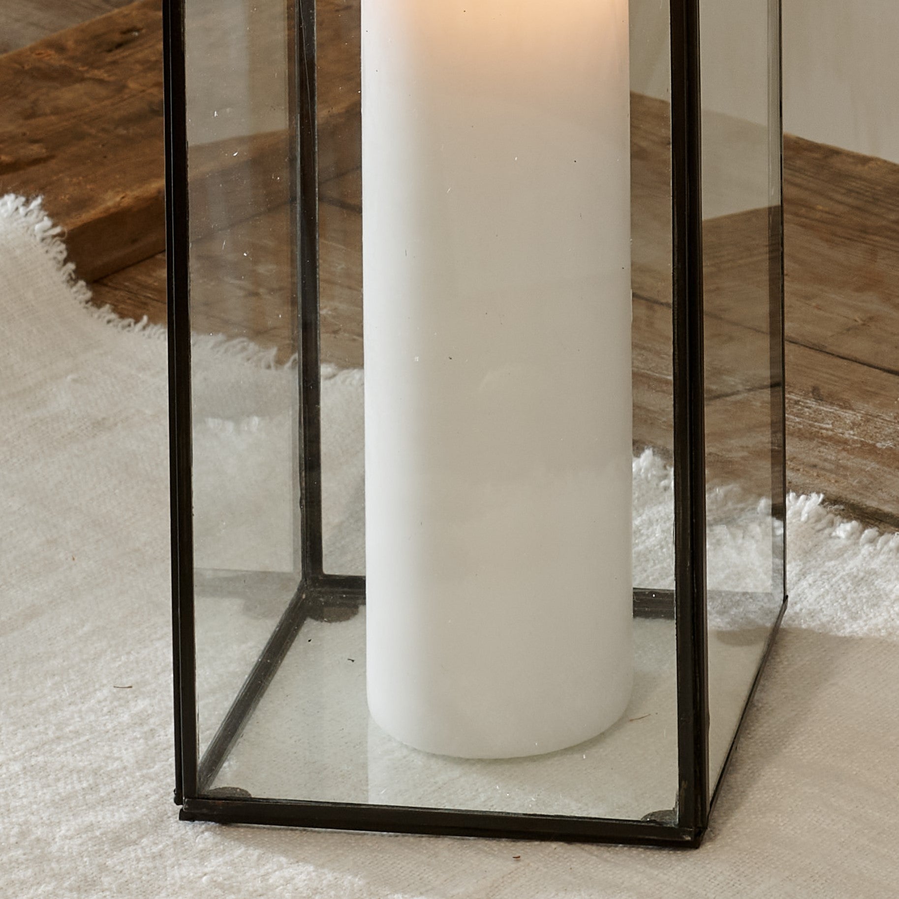 Close up of base of tall black candle lantern terrarium on cotton runner on wooden table