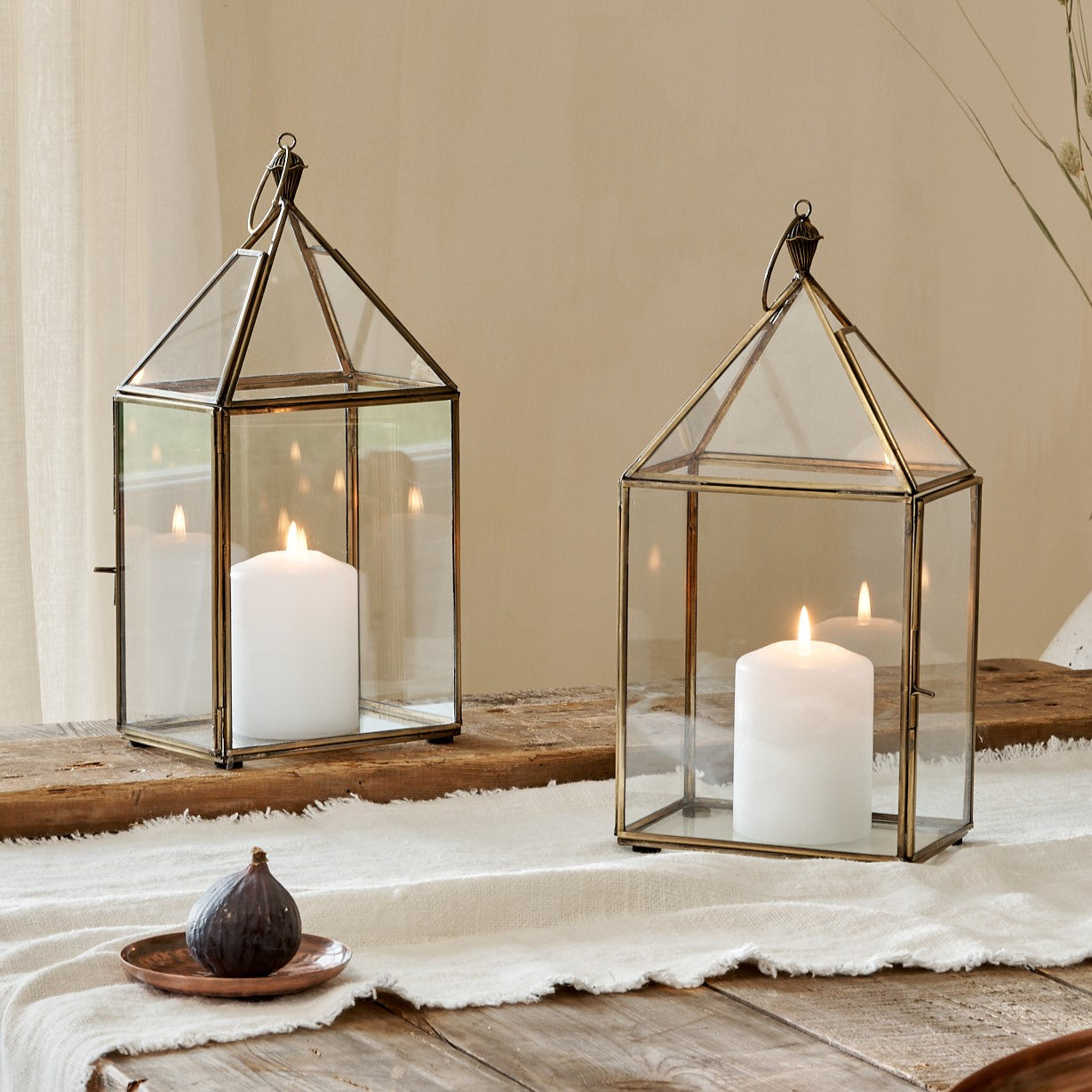 Small glass and brass candle lanterns on cotton runner on wooden table, with copper tray and coaster