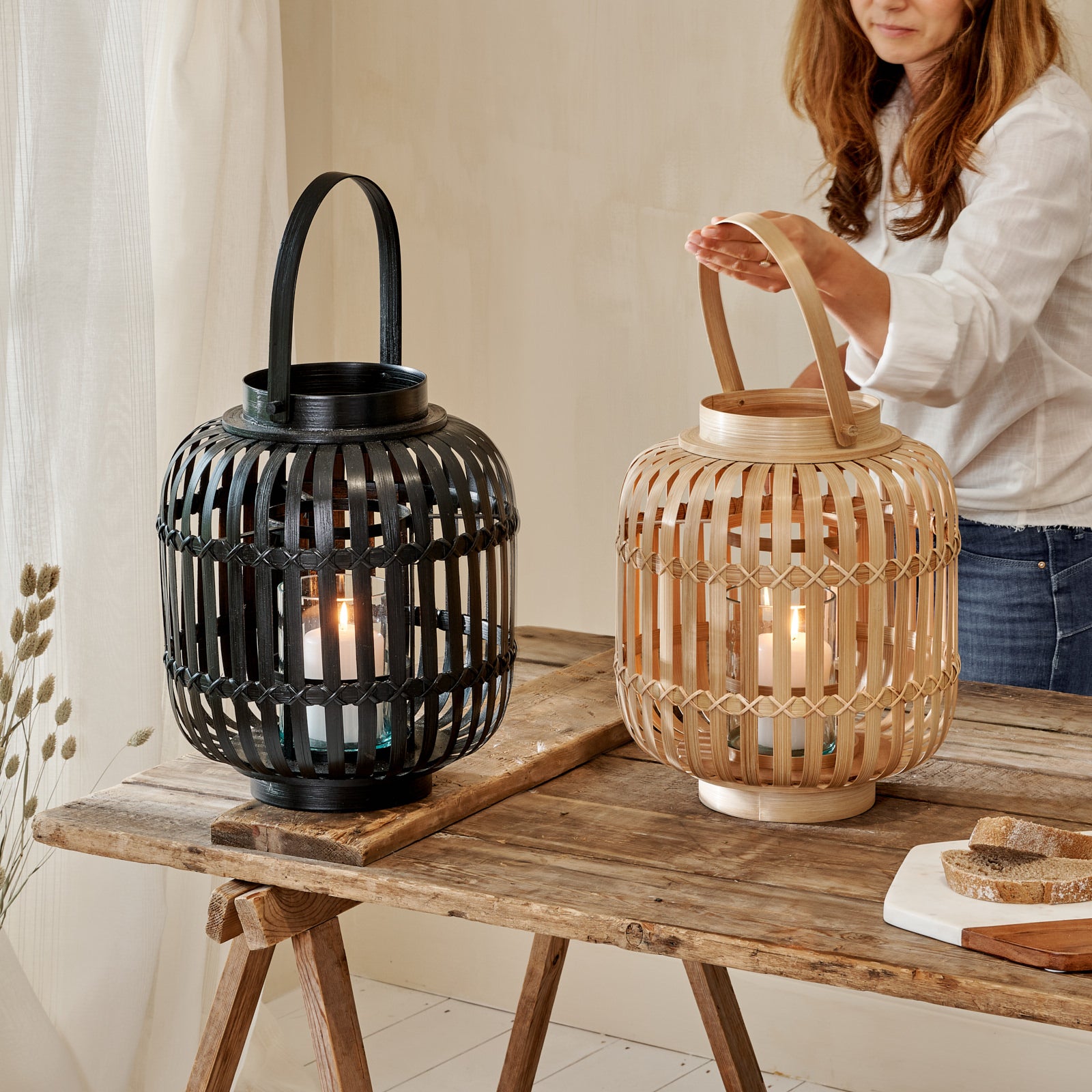 Black and natural bamboo hurricane lanterns on wooden table with woman holding handle