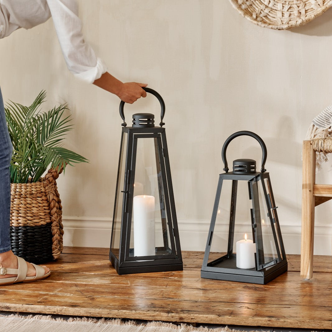black candle lanterns on wooden floor with chair and wicker basket, with woman holding handle