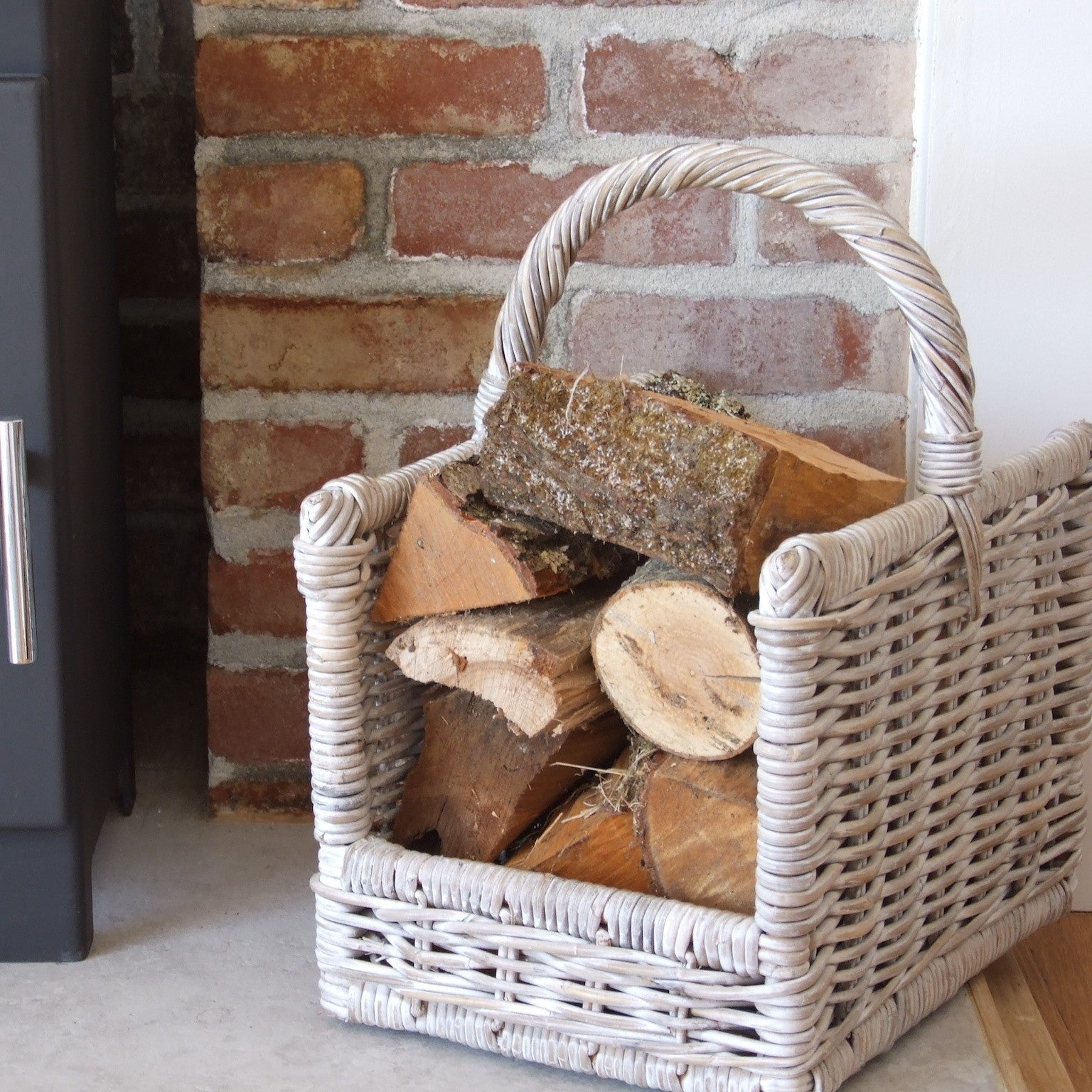 Wicker log basket full of logs in front of brick wall, next to fireplace