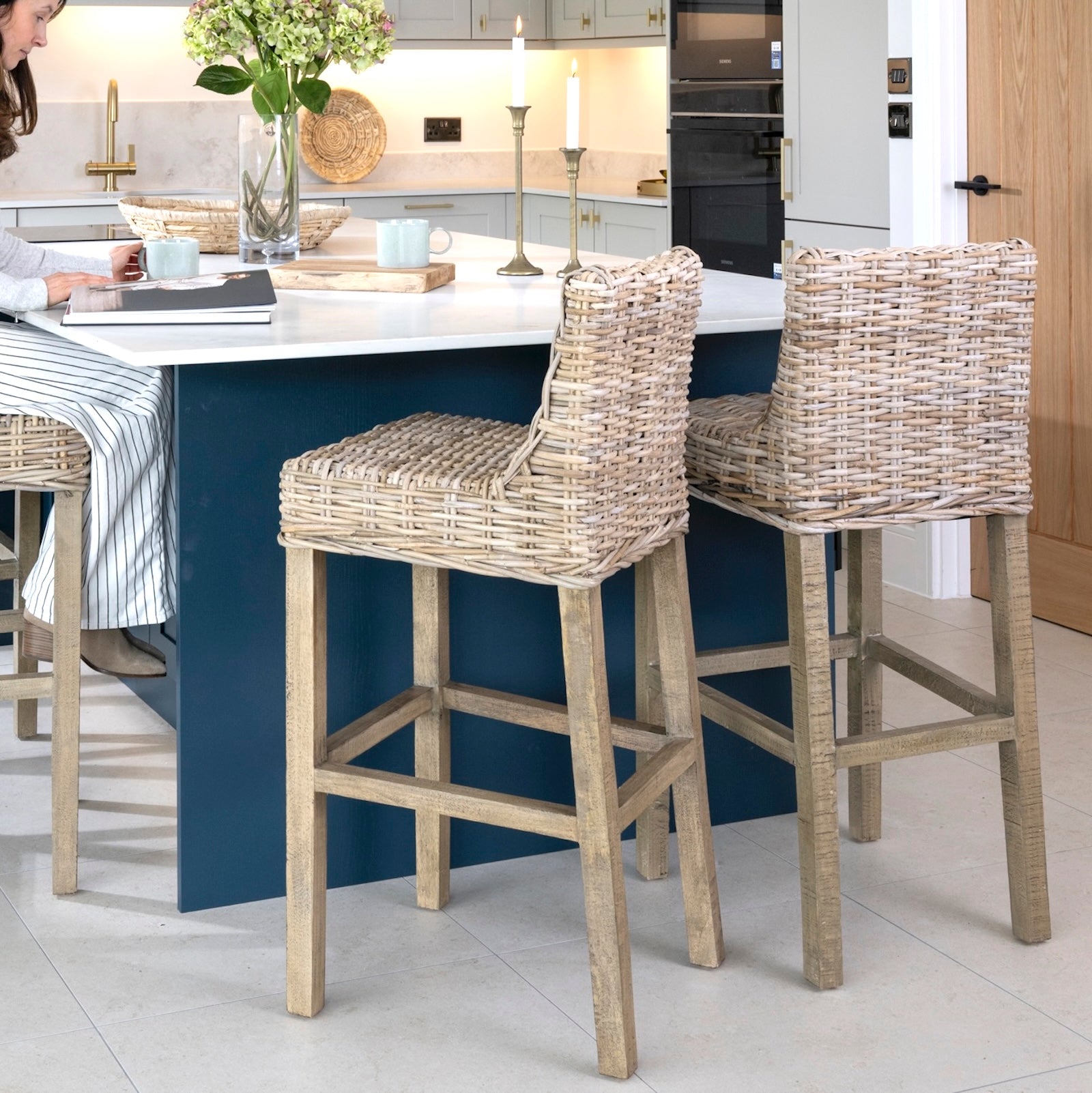 Kitchen with wicker bar stools at a counter, person sitting at the island and reading a book.