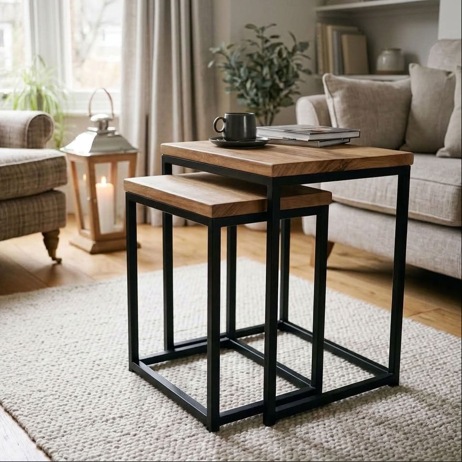 Two wooden nesting side tables in a living room setting. The tables feature light brown wooden tops and thick, open black metal frames.