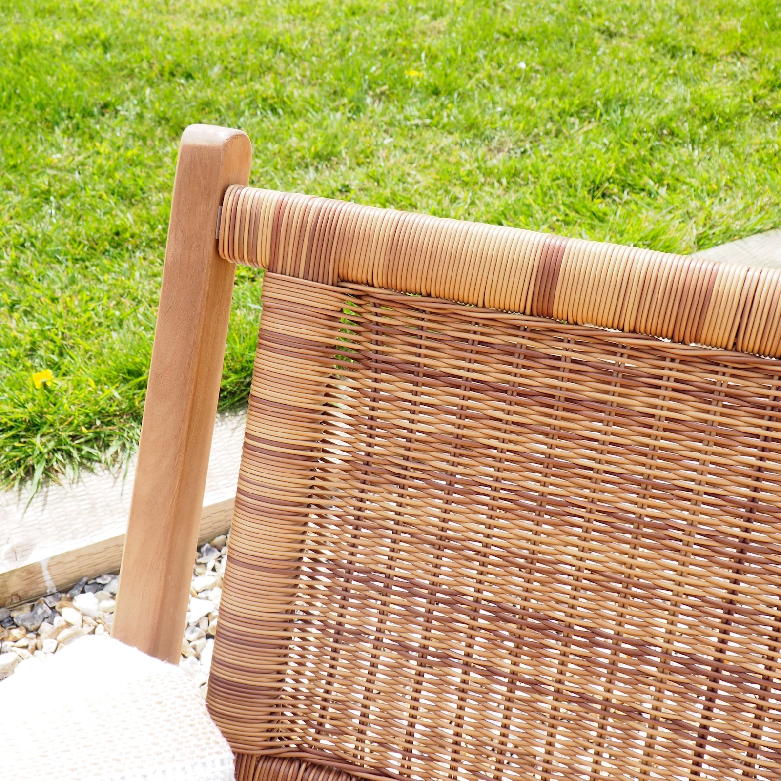 Close-up of an outdoor woven chair back with a natural wicker or rattan pattern and a light wood frame, set against a green grass background.