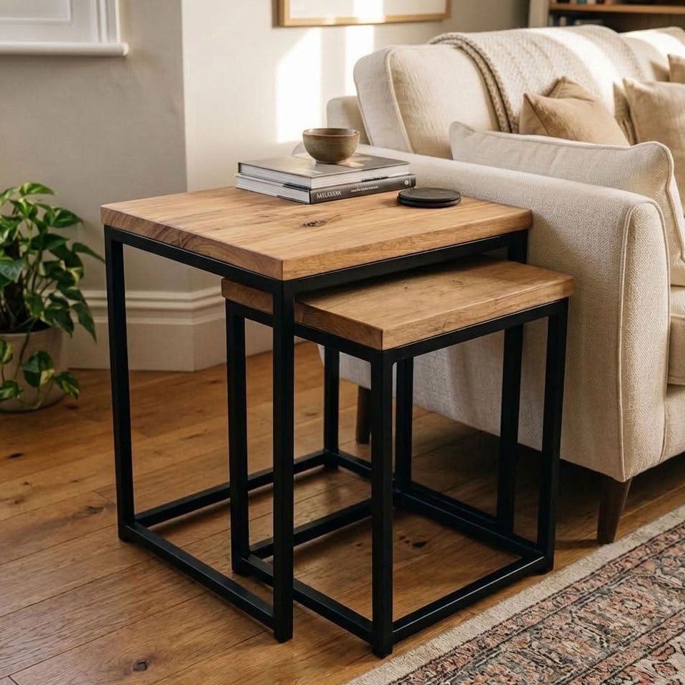 A pair of sold wood square nesting side tables with wood tops and black metal frames, styled in a cosy living room next to a cream sofa.
