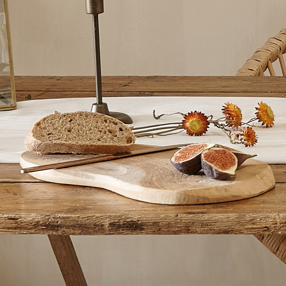Rustic wood serving board on wooden table with figs and flowers
