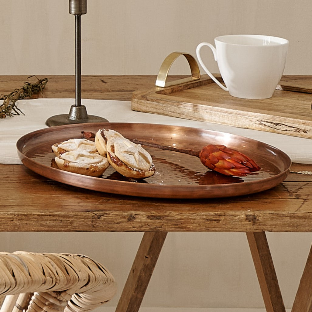 Round copper serving tray on wooden table, with mince pies and flower