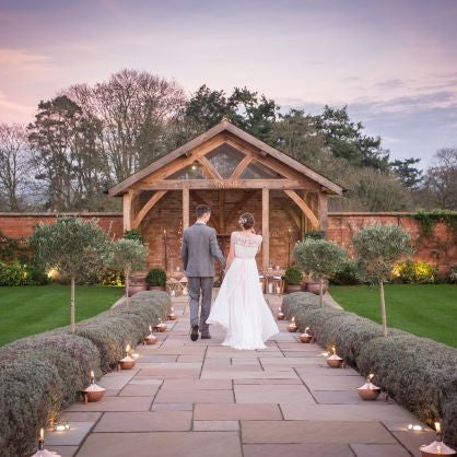 Outdoor wedding setting, with bride and groom and copper garden oil lamps lighting the isle