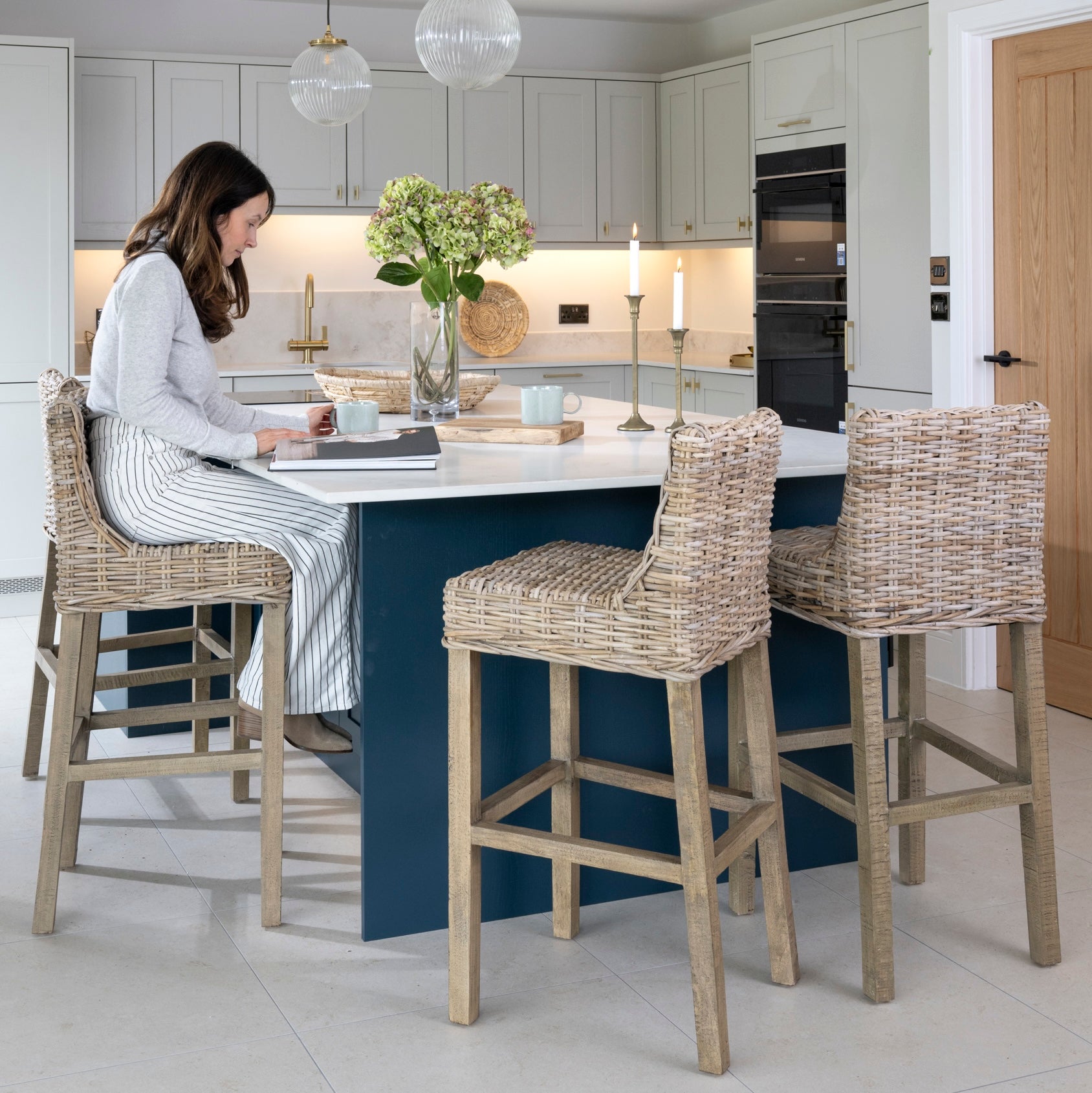modern kitchen with island, lady sat at island with rattan kitchen stools