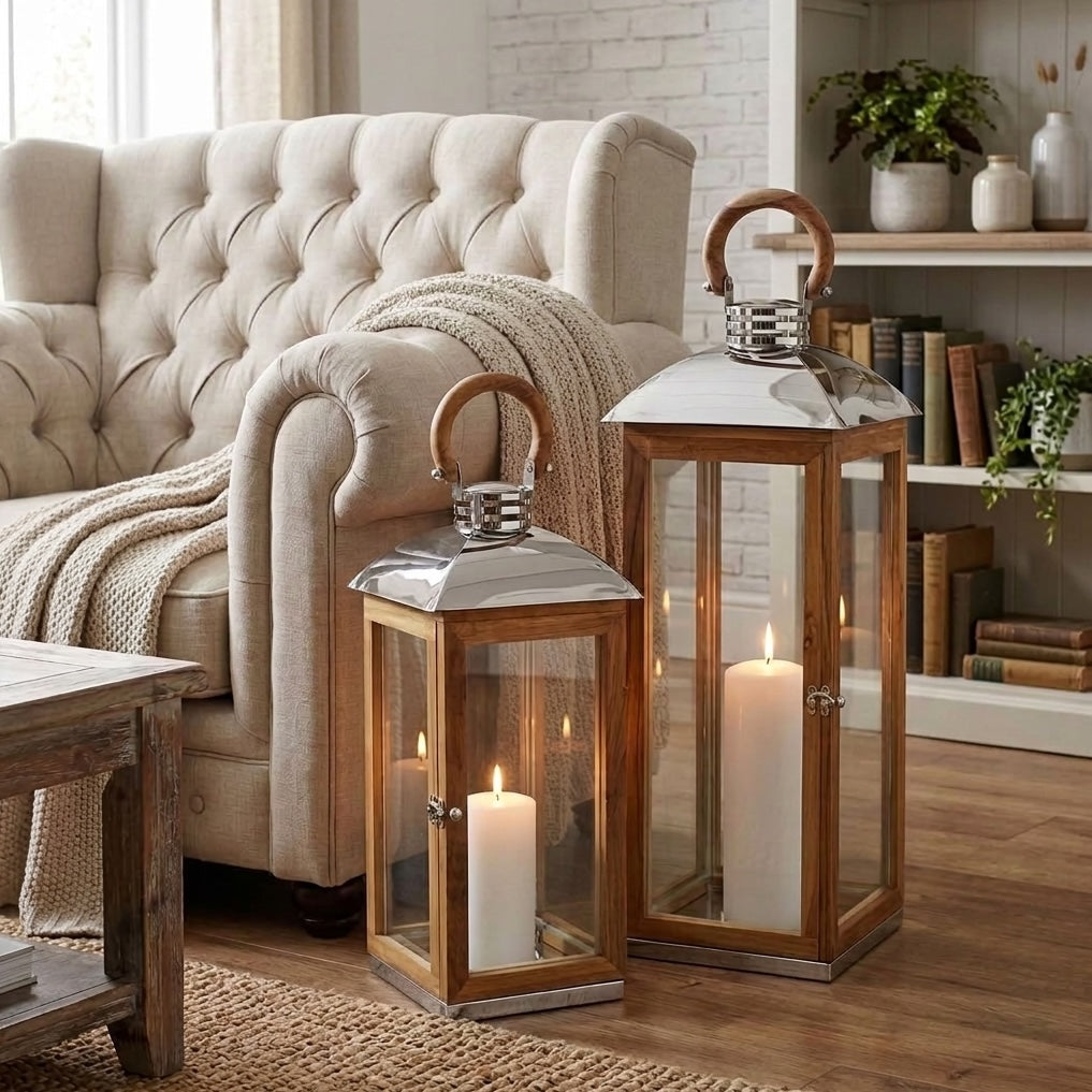 Two wooden lantern candles with glass panels and metal tops are displayed in a cozy neutral living room setting next to a cream armchair.