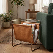 leather magazine rack with brass metal frame, green sofa with plants in the background