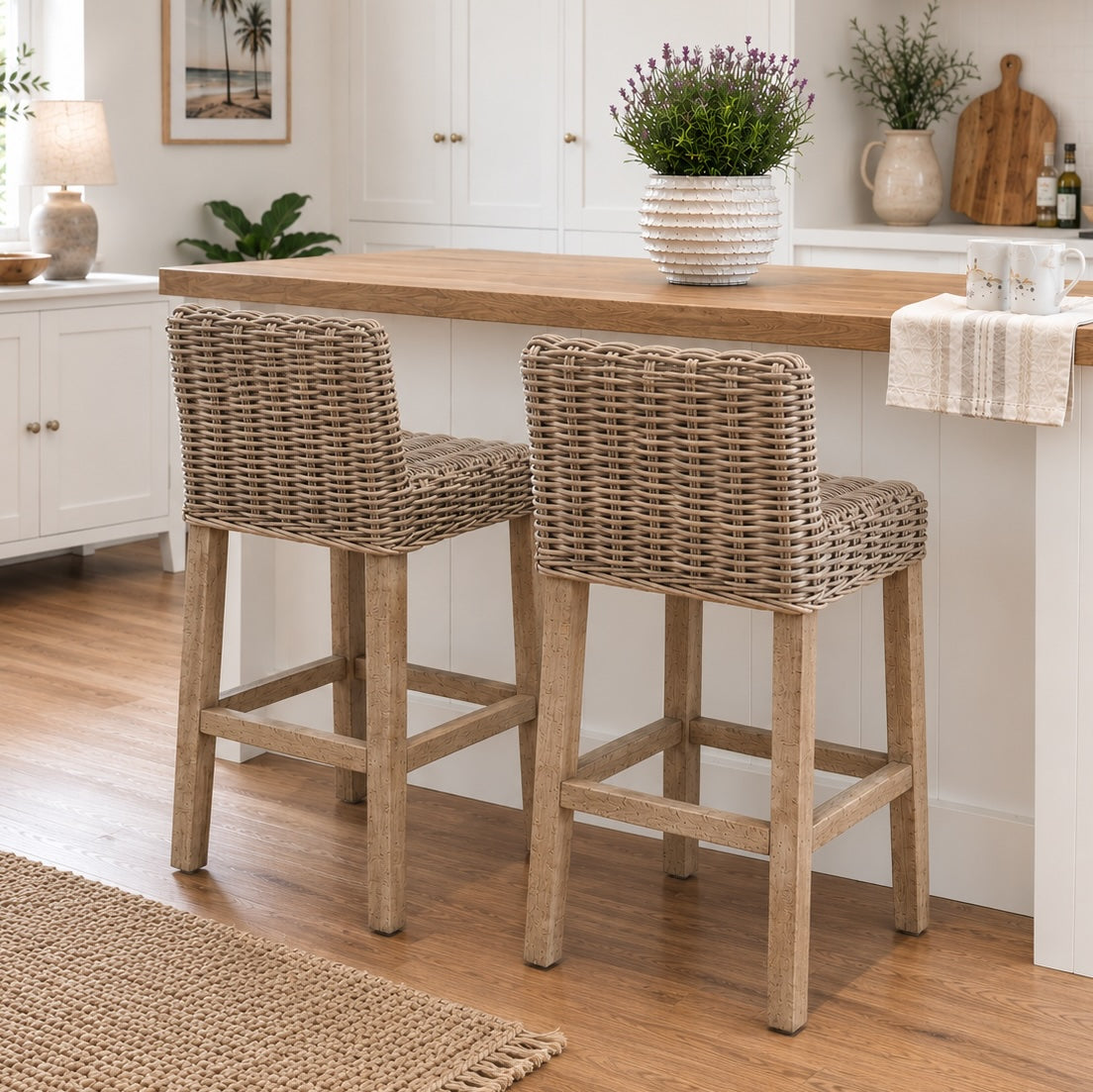 Two woven wicker bar stools with light wood legs, positioned at a kitchen island with a wooden countertop in a bright, modern kitchen.