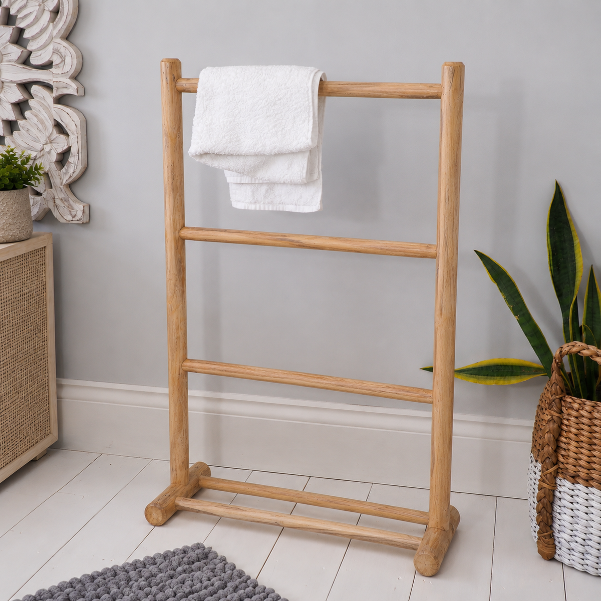 A natural light wood towel rack with four horizontal bars stands on a white tiled floor against a gray wall. A white towel is draped over the top bar.