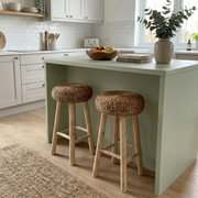 Two wicker bar stools in front of a kitchen island with a bowl of fruit on a windowsill.